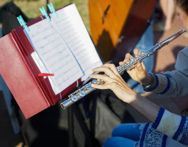 The girl is holding a large concert flute (in hands close-up). Professional musician at the rehearsal. A woman plays the transverse flute. closeup of hands of a musician playing the flute