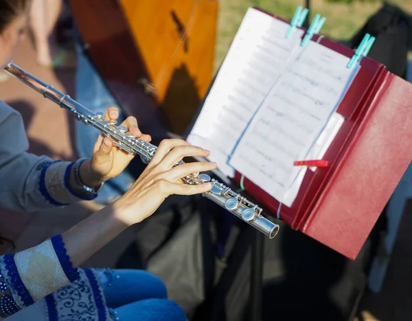 The girl is holding a large concert flute (in hands close-up). Professional musician at the rehearsal. A woman plays the transverse flute. closeup of hands of a musician playing the flute