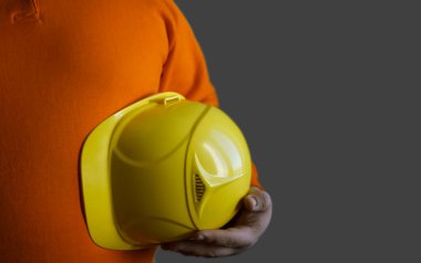 Kolunun altında sarı kask tutan mühendis ya da işçi beyaz, gri arka planda izole edilmiş. Yüzü yok. Yazı için boş kopyalama alanı. Tanımlanamayan kişi.