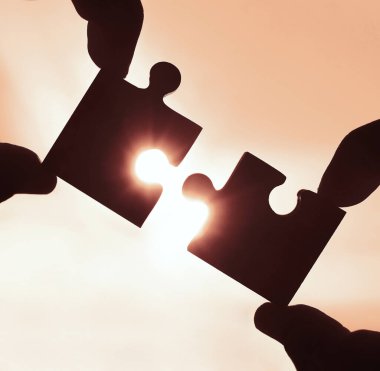 Gökyüzü arka planında yapboz parçaları olan eller.  