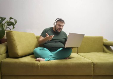 Ciddi sakallı, dizüstü bilgisayarlı, kablosuz kulaklıklı ve günlük kıyafetleriyle koltukta tek başına oturmuş en sevdiği müziği dinleyen bir erkek. 