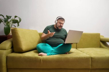 Ciddi sakallı, dizüstü bilgisayarlı, kablosuz kulaklıklı ve günlük kıyafetleriyle koltukta tek başına oturmuş en sevdiği müziği dinleyen bir erkek. 