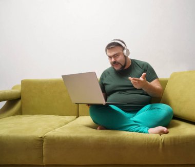 Ciddi sakallı, dizüstü bilgisayarlı, kablosuz kulaklıklı ve günlük kıyafetleriyle koltukta tek başına oturmuş en sevdiği müziği dinleyen bir erkek. 