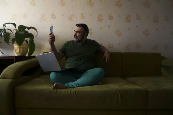 Ευτυχισμένος Γενειοφόρος Άνδρας Καστανά Μαλλιά Κάθεται Στον Καναπέ Και Χρησιμοποιώντας — Φωτογραφία Αρχείου