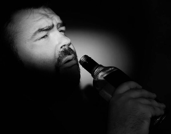 bearded Man with a hangover drinking jim or vodka - alcohol beverage from transparent glass bottle