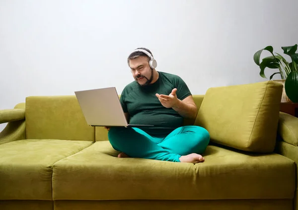 Hombre Barbudo Serio Con Portátil Auriculares Inalámbricos Ropa Casual Sentado —  Fotos de Stock