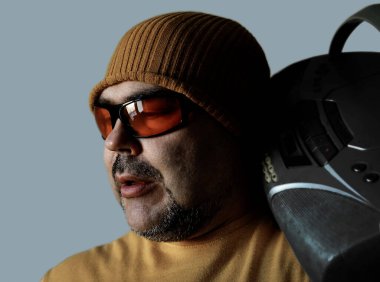 Pozitif ruh hali olan genç bir adamın fotoğrafı beyaz ya da gri arka planda izole edilmiş omuzlarında teyp taşıyor. Sarı şapkalı, güneş gözlüklü ve müzik dinleyen bir adam..