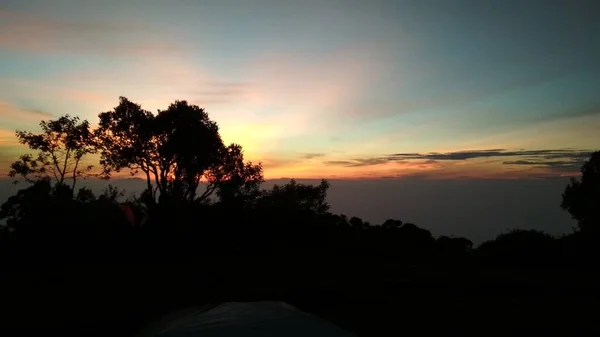 Bulutların arkasında gün doğumu ve sabah dağda ağaçlar