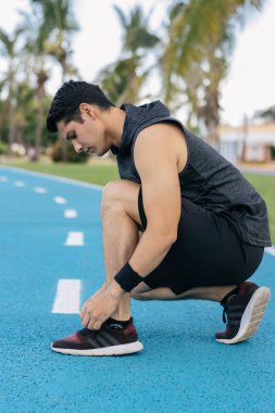 İspanyol genç yetişkin bir adam ayakkabı bağcıklarını bağlayıp aşağıya bakıyor.