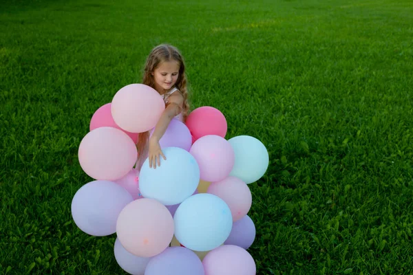 Malá krásná dívka s náručí plnou balónků na zelené trávě. — Stock fotografie
