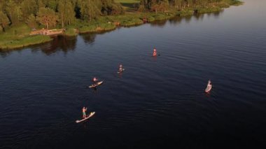 Gün batımında Stand Up Paddle 'da veya nehirde SUP sörf yapan insanların hava görüntüsü. Yaz tatilinde deniz kenarında su sporu yapan kadın ve erkeğin silueti. Sağlıklı yaşam tarzı Aktif turizm