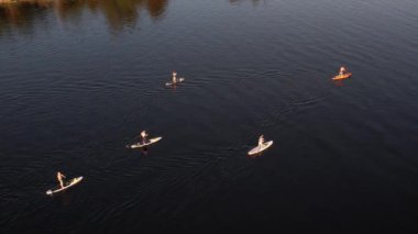 Gün batımında Stand Up Paddle 'da veya nehirde SUP sörf yapan insanların hava görüntüsü. Yaz tatilinde deniz kenarında su sporu yapan kadın ve erkeğin silueti. Sağlıklı yaşam tarzı Aktif turizm