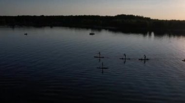 Gün batımında Stand Up Paddle 'da veya nehirde SUP sörf yapan insanların hava görüntüsü. Yaz tatilinde deniz kenarında su sporu yapan kadın ve erkeğin silueti. Sağlıklı yaşam tarzı Aktif turizm