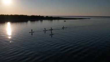 Gün batımında Stand Up Paddle 'da veya nehirde SUP sörf yapan insanların hava görüntüsü. Yaz tatilinde deniz kenarında su sporu yapan kadın ve erkeğin silueti. Sağlıklı yaşam tarzı Aktif turizm