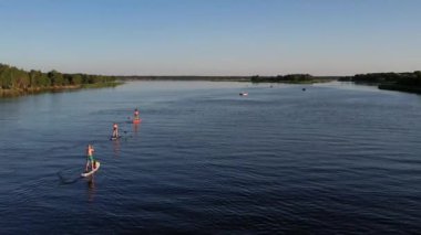 Gün batımında Stand Up Paddle 'da veya nehirde SUP sörf yapan insanların hava görüntüsü. Yaz tatilinde deniz kenarında su sporu yapan kadın ve erkeğin silueti. Sağlıklı yaşam tarzı Aktif turizm