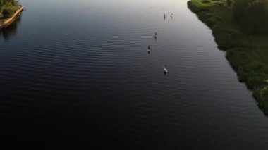 Aerial view of people riding on Stand Up Paddle or SUP Board in the river at sunset. Silhouette of man and female doing water sport during summer holidays on a sea. Healthy lifestyle. Active tourism