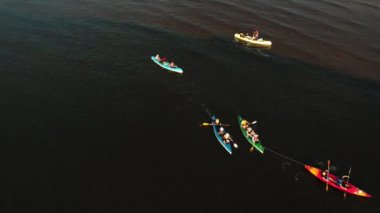 Gün batımında nehirde kayak yapan bir grup insanın hava aracı görüntüsü. Yaz tatilinde deniz kenarında su sporu yapan turistler. Akşamları kano sürerler. Sağlıklı bir yaşam tarzı. Etkin seyahat 