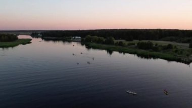 Gün batımında nehirde kayak yapan bir grup insanın hava aracı görüntüsü. Yaz tatilinde deniz kenarında su sporu yapan turistler. Akşamları kano sürerler. Sağlıklı bir yaşam tarzı. Etkin seyahat 