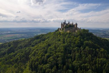 Drone shot of Hohenzollern Castle on forested mountain top in the Swabian Alps in summer. Scenic aerial view of old German Burg. Famous fairytale Gothic landmark in Stuttgart vicinity