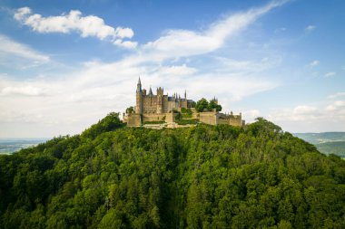 Drone shot of Hohenzollern Castle on forested mountain top in the Swabian Alps in summer. Scenic aerial view of old German Burg. Famous fairytale Gothic landmark in Stuttgart vicinity