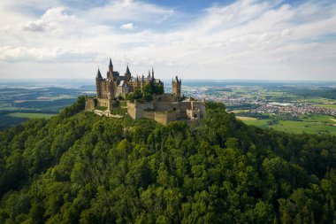 Drone shot of Hohenzollern Castle on forested mountain top in the Swabian Alps in summer. Scenic aerial view of old German Burg. Famous fairytale Gothic landmark in Stuttgart vicinity