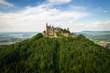 Drone shot of Hohenzollern Castle on forested mountain top in the Swabian Alps in summer. Scenic aerial view of old German Burg. Famous fairytale Gothic landmark in Stuttgart vicinity