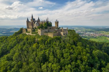 Drone shot of Hohenzollern Castle on forested mountain top in the Swabian Alps in summer. Scenic aerial view of old German Burg. Famous fairytale Gothic landmark in Stuttgart vicinity
