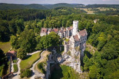 Yazın Swabian Alpleri 'ndeki orman kayalıkları üzerindeki lichtenstein kalesinin (Schloss) havadan görünüşü. Gökyüzünde Gotik diriliş tarzında romantik masal sarayının mevsimsel manzarası. Avrupa 'nın ünlü simgesi