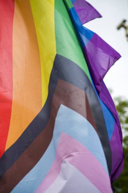 Close-Up rainbow gay pride flag outside on a street. Symbol of the Lesbian Bisexual Transgender LGBT community waving in wind against cloudy sky. Social movement for freedom and equliaty. Copy Space 
