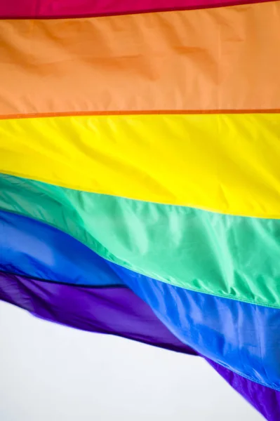 Close-Up rainbow gay pride flag outside on a street. Symbol of the Lesbian Bisexual Transgender LGBT community waving in wind against cloudy sky. Social movement for freedom and equliaty. Copy Space