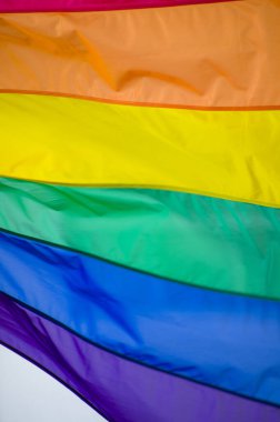 Close-Up rainbow gay pride flag outside on a street. Symbol of the Lesbian Bisexual Transgender LGBT community waving in wind against cloudy sky. Social movement for freedom and equliaty. Copy Space 