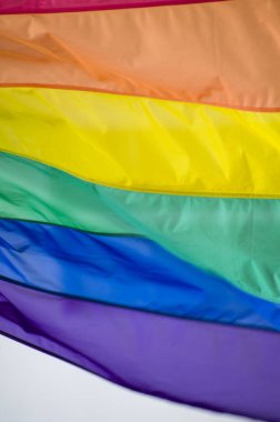 Close-Up rainbow gay pride flag outside on a street. Symbol of the Lesbian Bisexual Transgender LGBT community waving in wind against cloudy sky. Social movement for freedom and equliaty. Copy Space 
