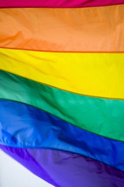 Close-Up rainbow gay pride flag outside on a street. Symbol of the Lesbian Bisexual Transgender LGBT community waving in wind against cloudy sky. Social movement for freedom and equliaty. Copy Space 
