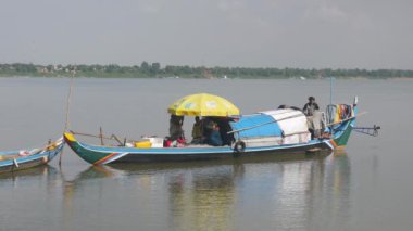 Kampong Cham - Kamboçya - 07 - 10 - 2019: balıkçılar teknede oturur ve çamaşır ipine çamaşır asan bir kadın tarafından elle balık ağı tamir edilir. 