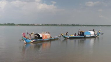 Kampong Cham - Kamboçya - 07 - 10 - 2019; balıkçı balıkçı teknede şemsiye açarken çamaşır ipinde çamaşırlarını asan bir kadın 
