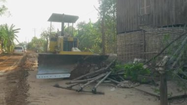 Kampong - Kamboçya - 03 - 12 - 2019: Küçük buldozer ağaç kütüklerini ve diğer odun döküntülerini Stilt-house 'un önünden kaldırıyor