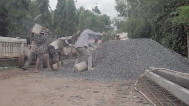 Kampong - Kamboçya - 04-09 - 2018; bir grup işçi kovalara çakıl doldurup bir çimento karıştırıcısına koyuyorlar 