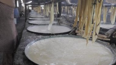  Sıcak soya sütü soğuduğunda, yüzeyinde ince bir katman oluşur, onu ikiye bölmek için bıçak kullanan bir işçi ve sonra ince çarşafları bir bambu şeridine sarkıtır (yakın çekim).)