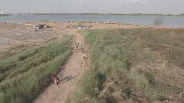 Bir grup turistin bisikletlerini iterken çekilen hava aracı görüntüleri. Arka planda nehrin üzerindeki bambu köprü. 
