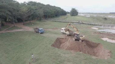 Kampong - Cambodia - 03 -12 - 2019 :  Drone shot of small truck loaded with earth leaves while an excavator loading earth into another truck in open field