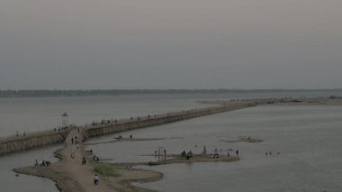 Gece vakti bir bambu köprüsünden geçen insan ve araçların nehir kenarını görüntüle 