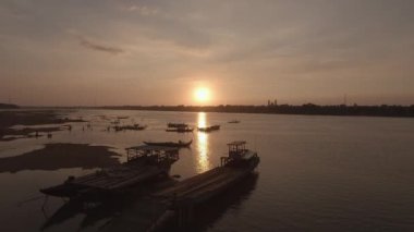 Düşük su mevsiminde, gün batımında, teknelerin etrafında yüzen insanların siluetlerini gösteren insansız hava aracı görüntüleri.. 