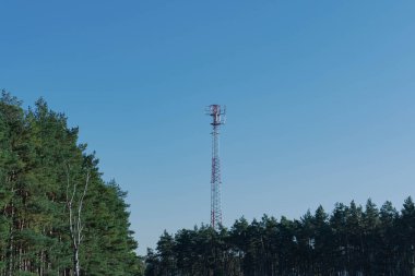 Direk, cep telefonu için merkez istasyon. Metal yapı beyaz ve kırmızıya boyanmıştır. Tepesinde anten olan bir taç. Gökyüzü açık..