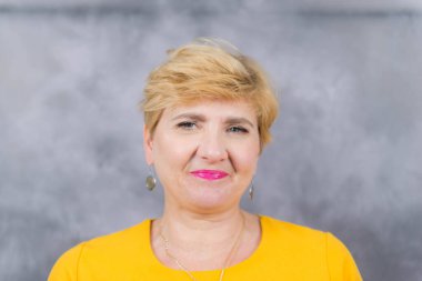 Çekici, orta yaşlı, kısa sarı saçlı bir kadın. Sarı bir Midi elbisesi giymişti. Fotoğraf gri bir arkaplanda çekildi..