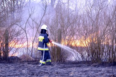 Yangın yerinde yangın söndürme eylemi. Bir itfaiyeci yangını söndürüyor. Sıcak hava ve dumanın yansıması görüntüyü bulanıklaştırıyor.