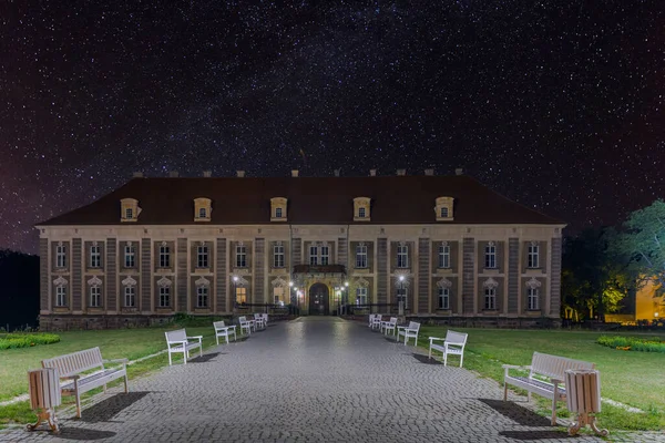 夜にポーランドの裁判所宮殿 暗闇は電気ランタンの明かりで照らされています 宮殿の上には雲一つない星に覆われた空があります — ストック写真