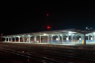 Tren istasyonu, gece demiryolu platformları, elektrik fenerleriyle aydınlatılıyor. Bulutsuz gökyüzünde yıldızları görebilirsin..