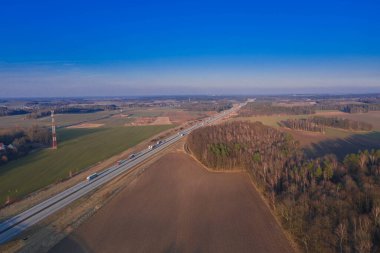 Geniş bir düzlük, tarıma elverişli tarlalar ve aralarında gri asfalt bir yol görebileceğiniz çayırlar. Güneşli bir gün. Arabalar yolda gidiyor. İHA 'dan fotoğraf..