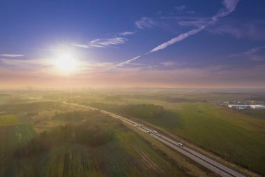 Geniş bir düzlük, tarıma elverişli tarlalar ve aralarında gri asfalt bir yol görebileceğiniz çayırlar. Güneşli bir gün. Arabalar yolda gidiyor. İHA 'dan fotoğraf..