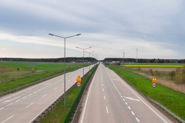 Güneşli bir gün. Gökyüzü biraz bulutlu, ovalar ekilebilir tarlalar ve çayırlarla kaplı. Ovada iki şeritli beton bir yol var. Üzerinde giden arabaları görebilirsin..
